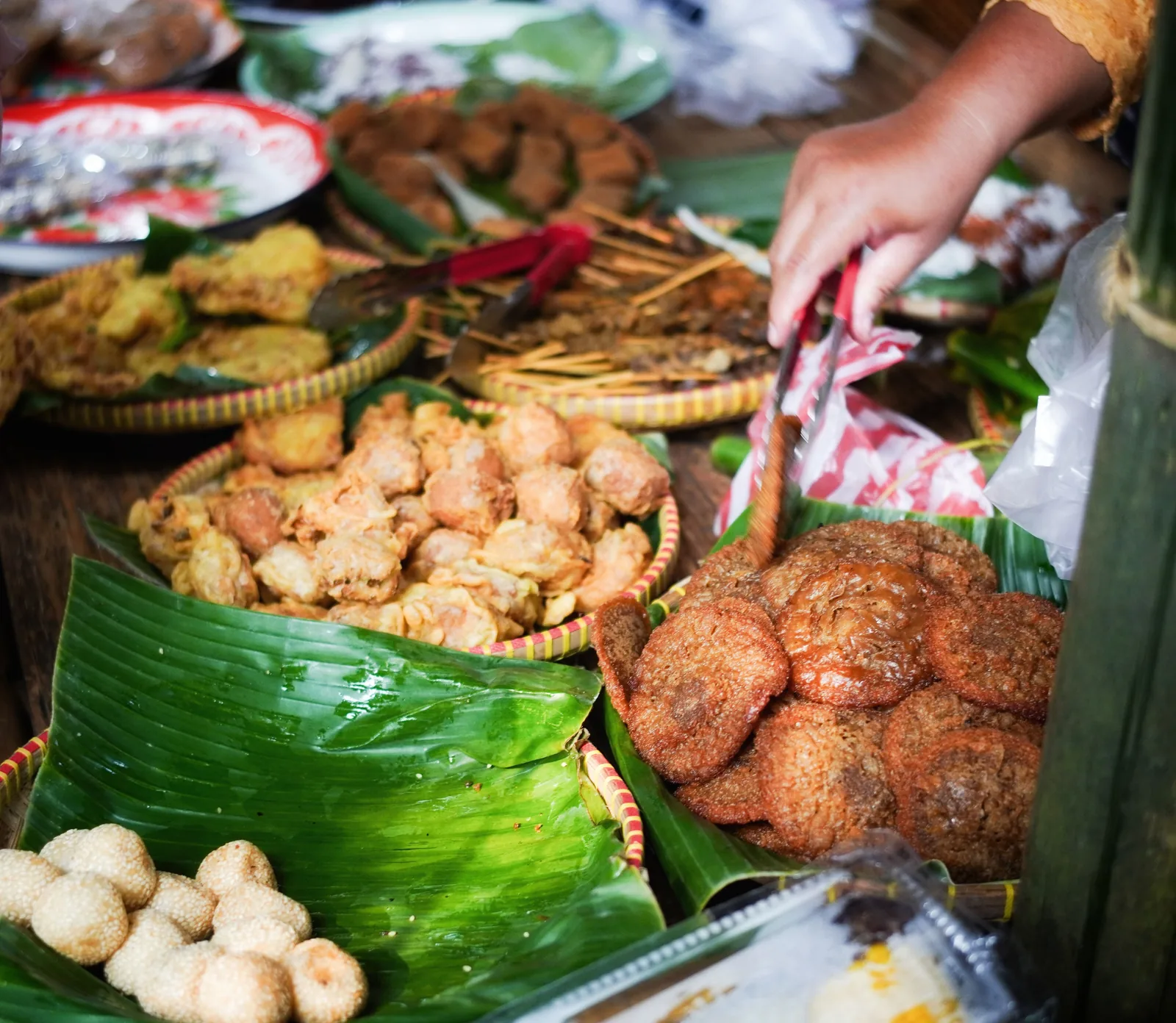 Hands serving Indonesian fried snacks on a banana leaf