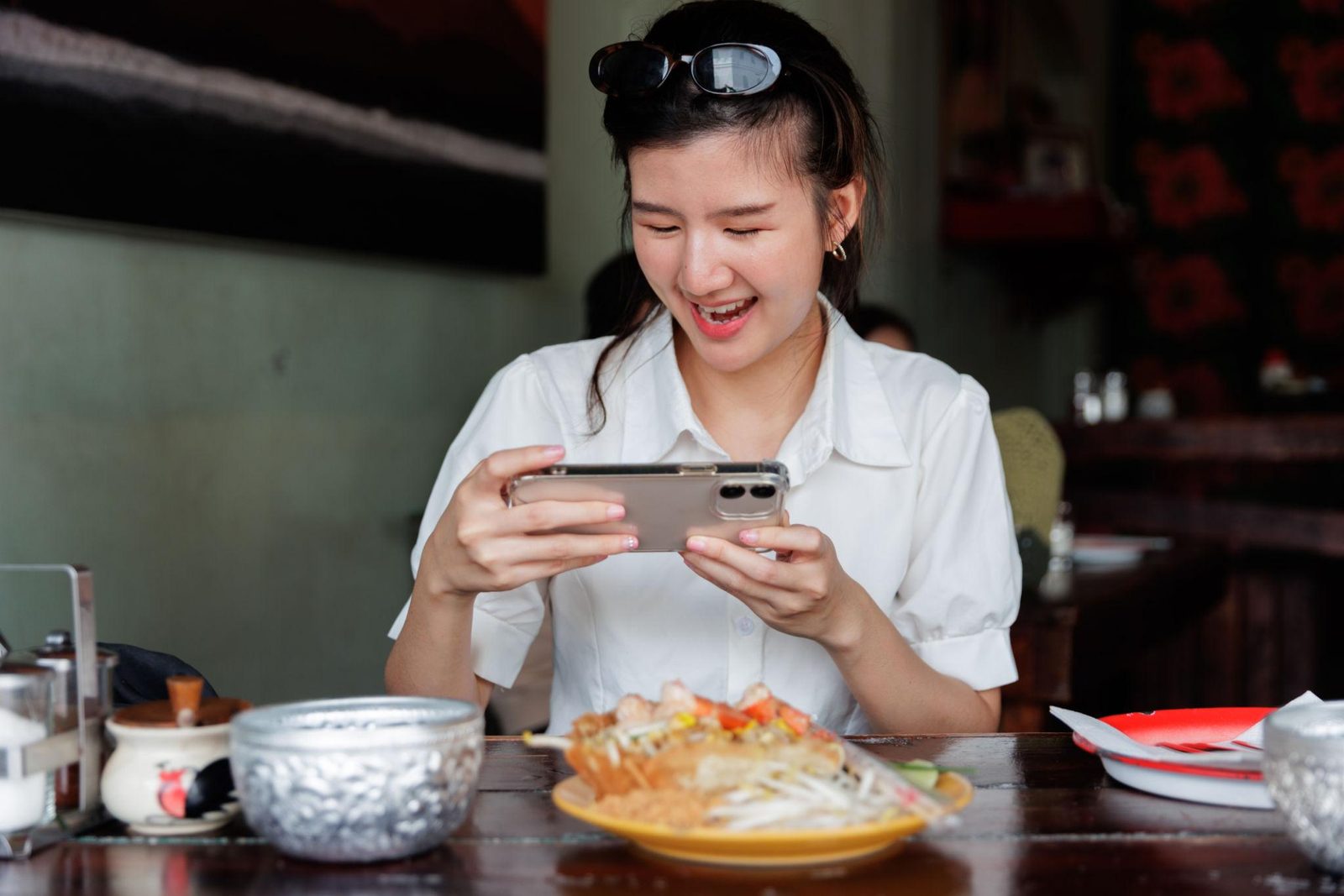 Woman photographing a plate of pad Thai with her phone before eating