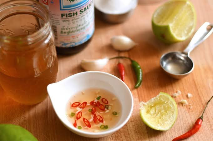 Close-up of a bottle of nuoc mam fish sauce with a dipping bowl, garlic, chili, and lime