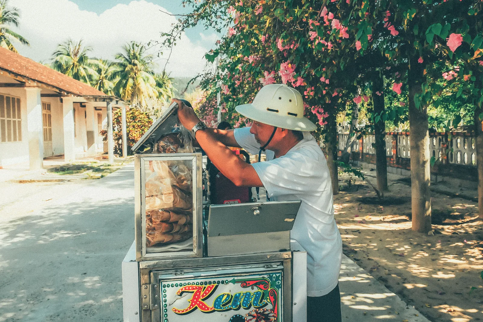 Vietnamese street vendor in conical hat carrying food baskets at a market stall