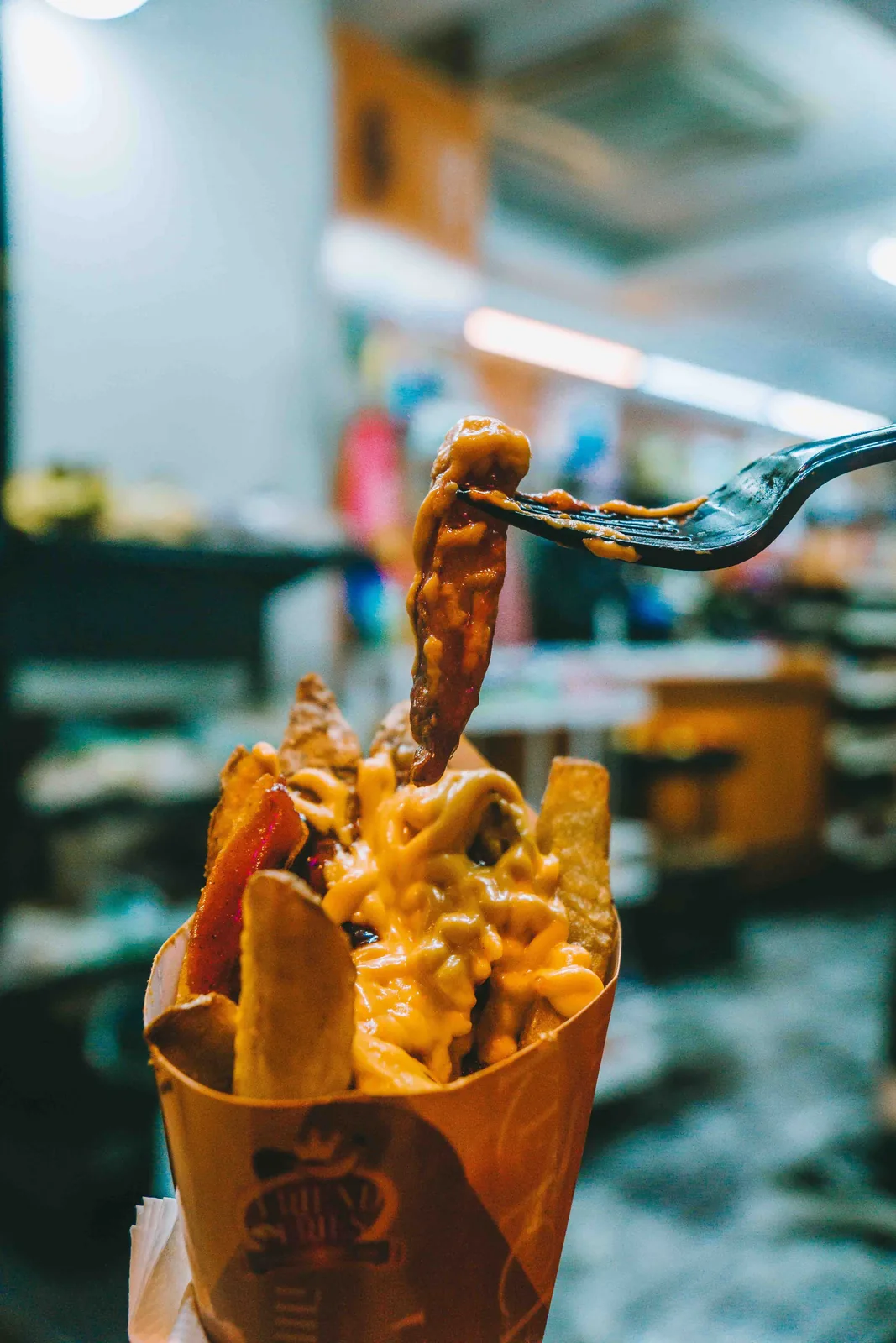 Hand holding a cup of fries with sauce